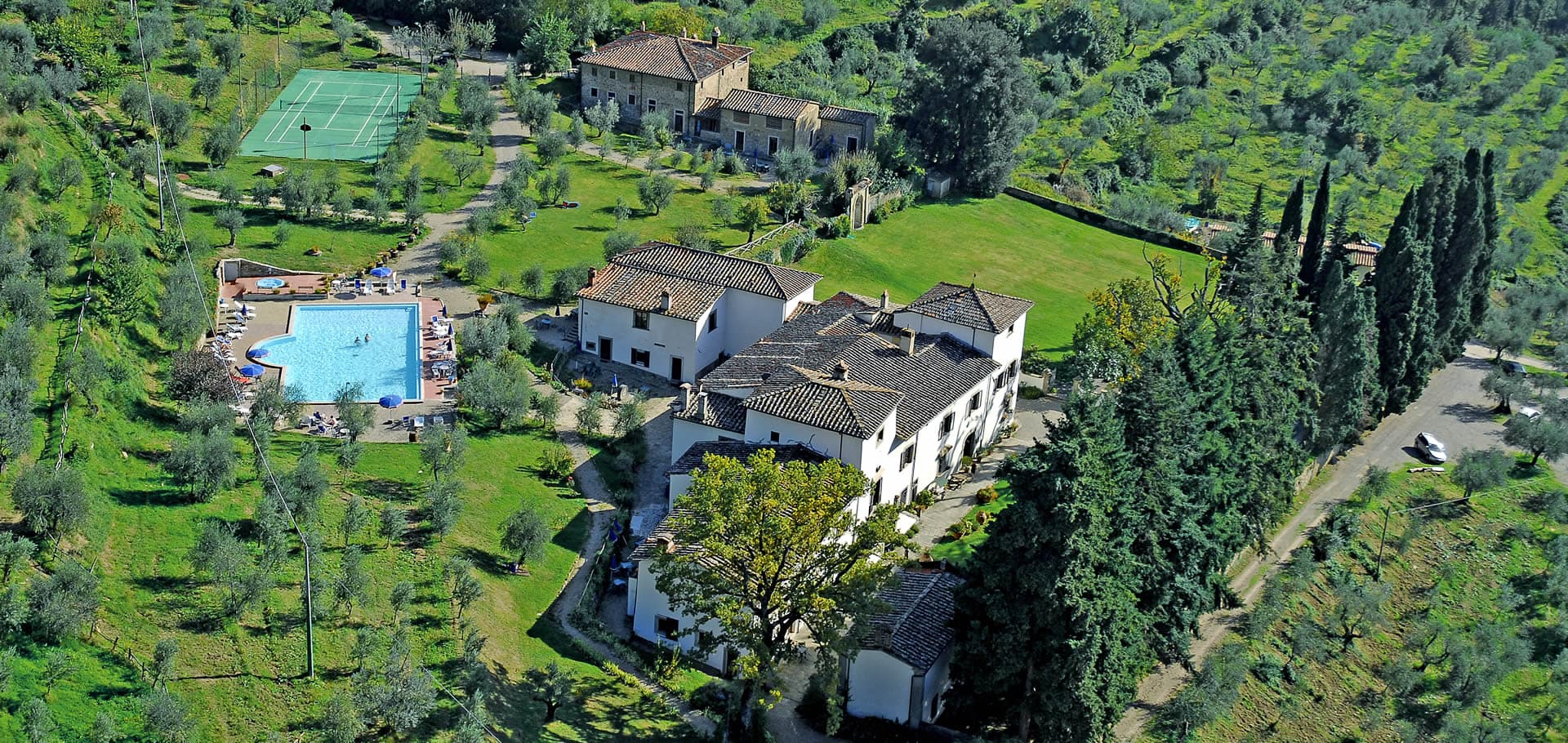 Aerial view of Villa Grassina, showing the villa buildings, swimming pool, tennis court and olive groves on a Tuscan hillside