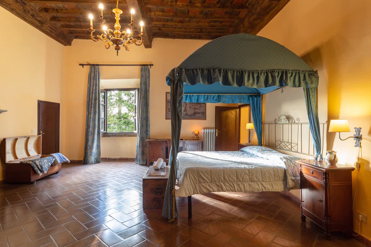 A bedroom in the main villa, with a canopy bed, a chandelier under a painted beamed ceiling, and terracotta floors